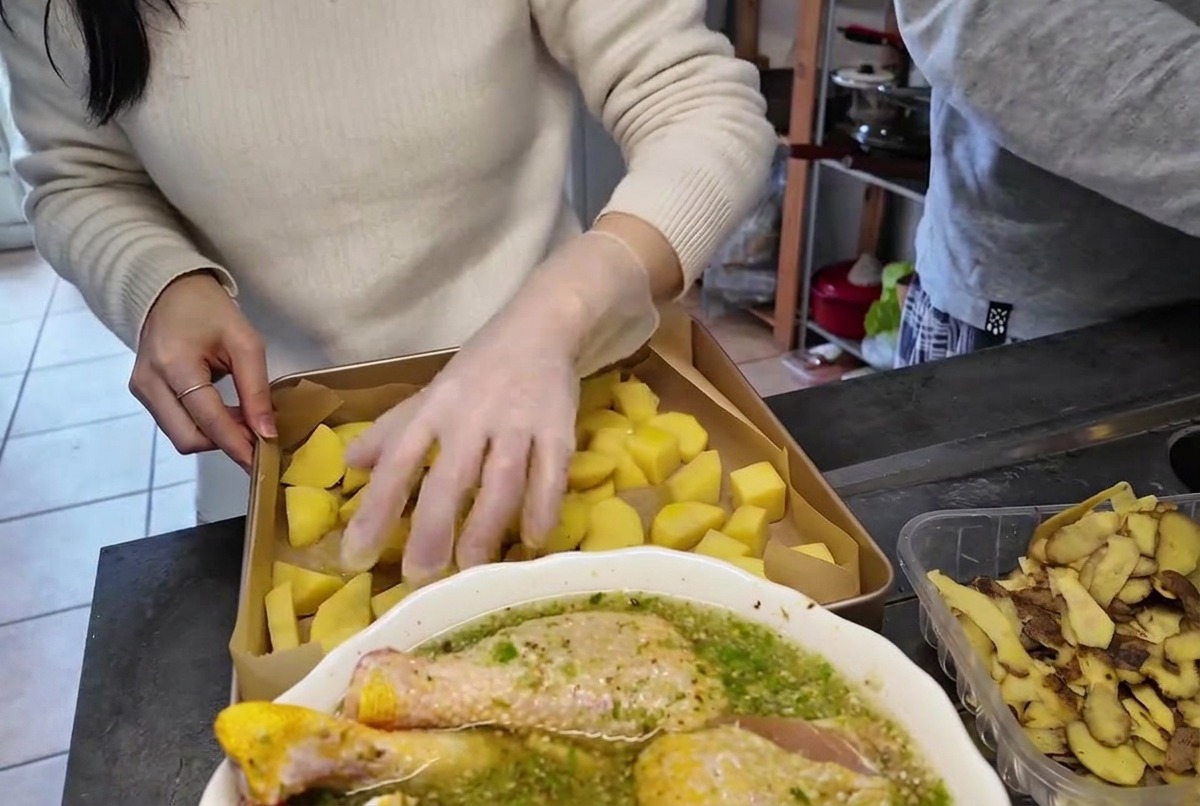 Une main avec un gant en plastique transparent qui mélange des morceaux de pommes de terre dans un plat de cuisson en métal.