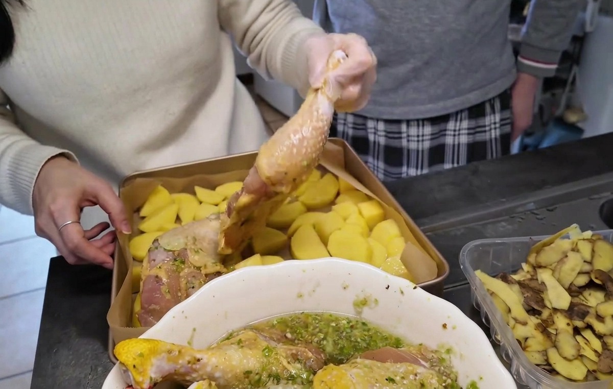 Cuisses de poulet crues et marinées disposées côté peau vers le haut sur une couche de pommes de terre coupées dans un plat de cuisson doré.