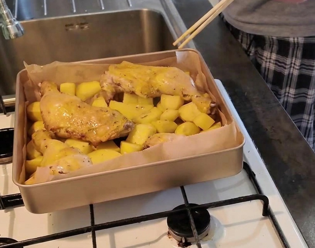 Une personne pique la chair dune cuisse de poulet posée sur des pommes de terre à laide de baguettes pour vérifier sa cuisson.