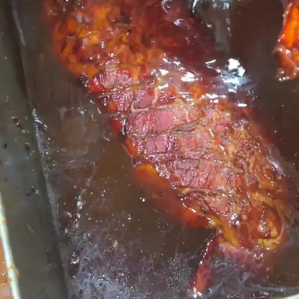 Un travers de porc rôti et doré généreusement arrosé dun sirop de miel riche et brillant dans un plateau en inox.