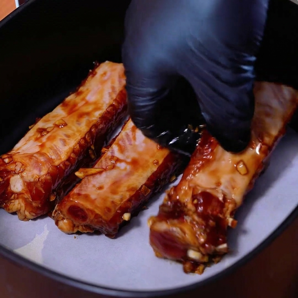 Ribs de porc marinés alignés côte à côte sur du papier cuisson dans le panier dune friteuse sans huile.