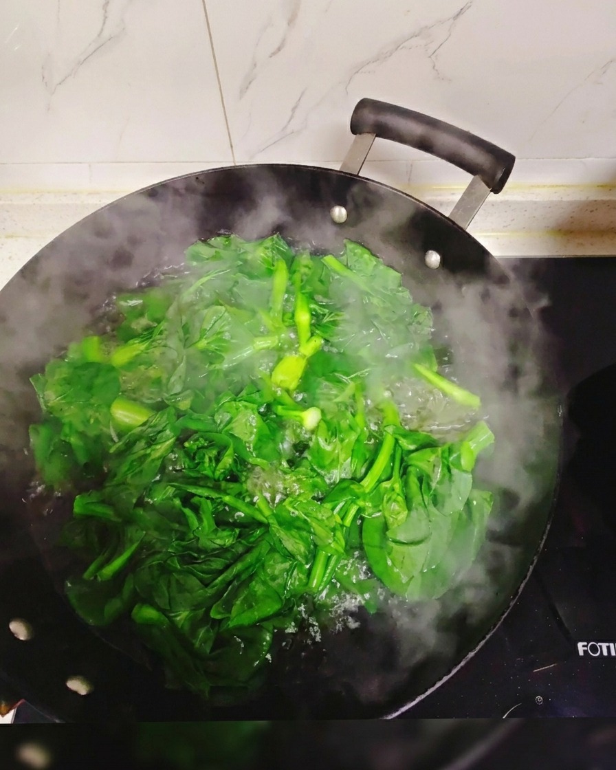 Des légumes verts à feuilles fraîches plongés et blanchis dans un grand wok rempli deau bouillante et fumante.