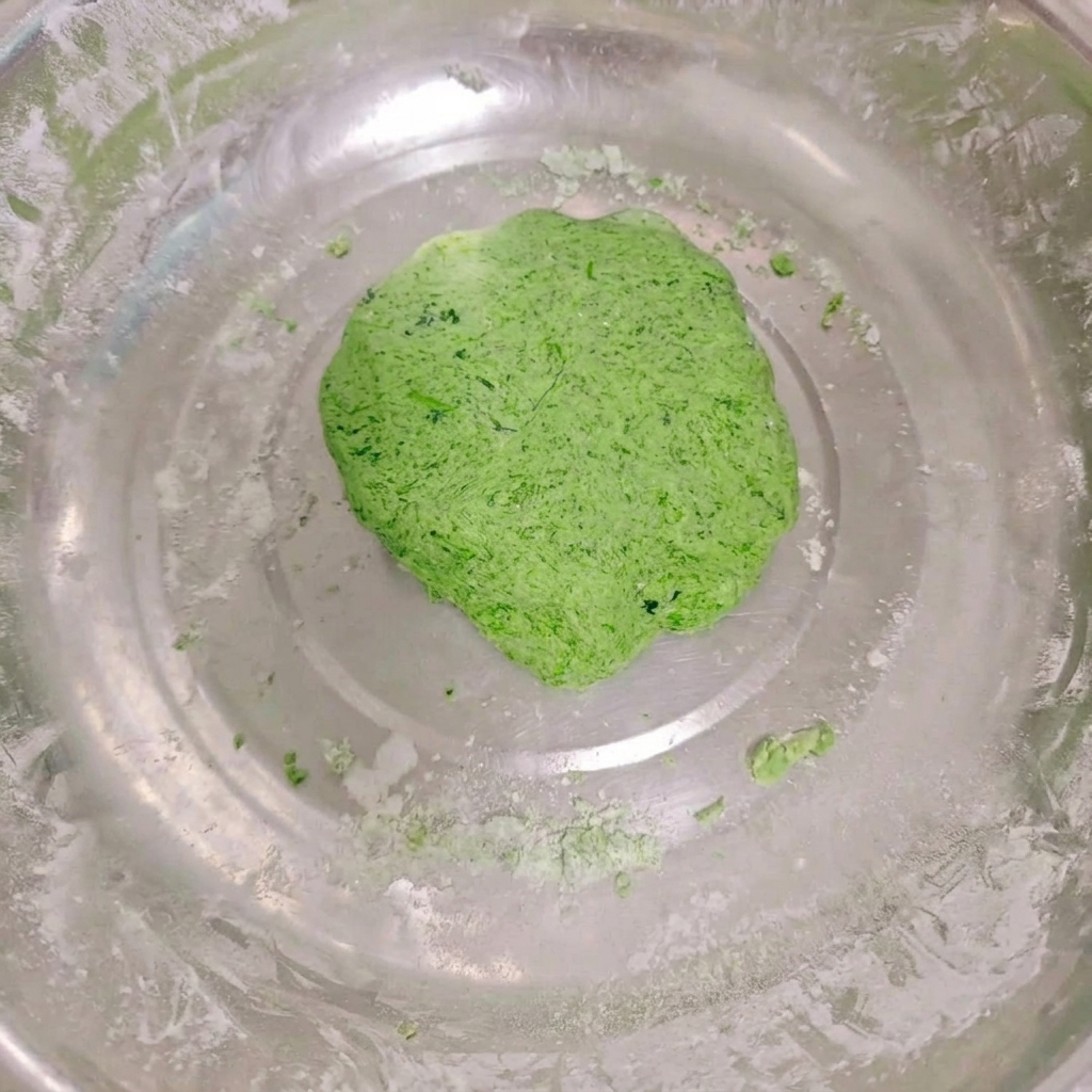 Une boule de pâte de légumes lisse et dun vert éclatant reposant dans un grand bol en acier inoxydable.