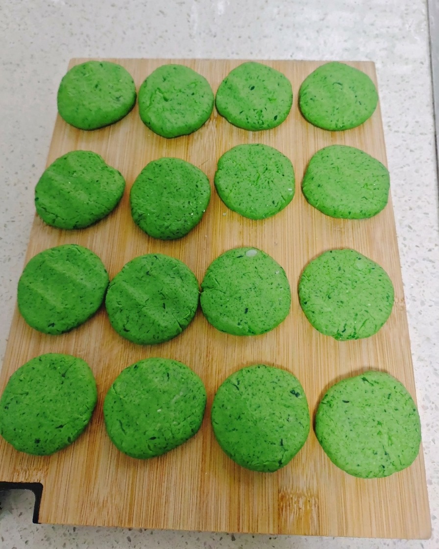 Seize galettes rondes de légumes verts disposées de manière régulière sur une planche à découper en bois.