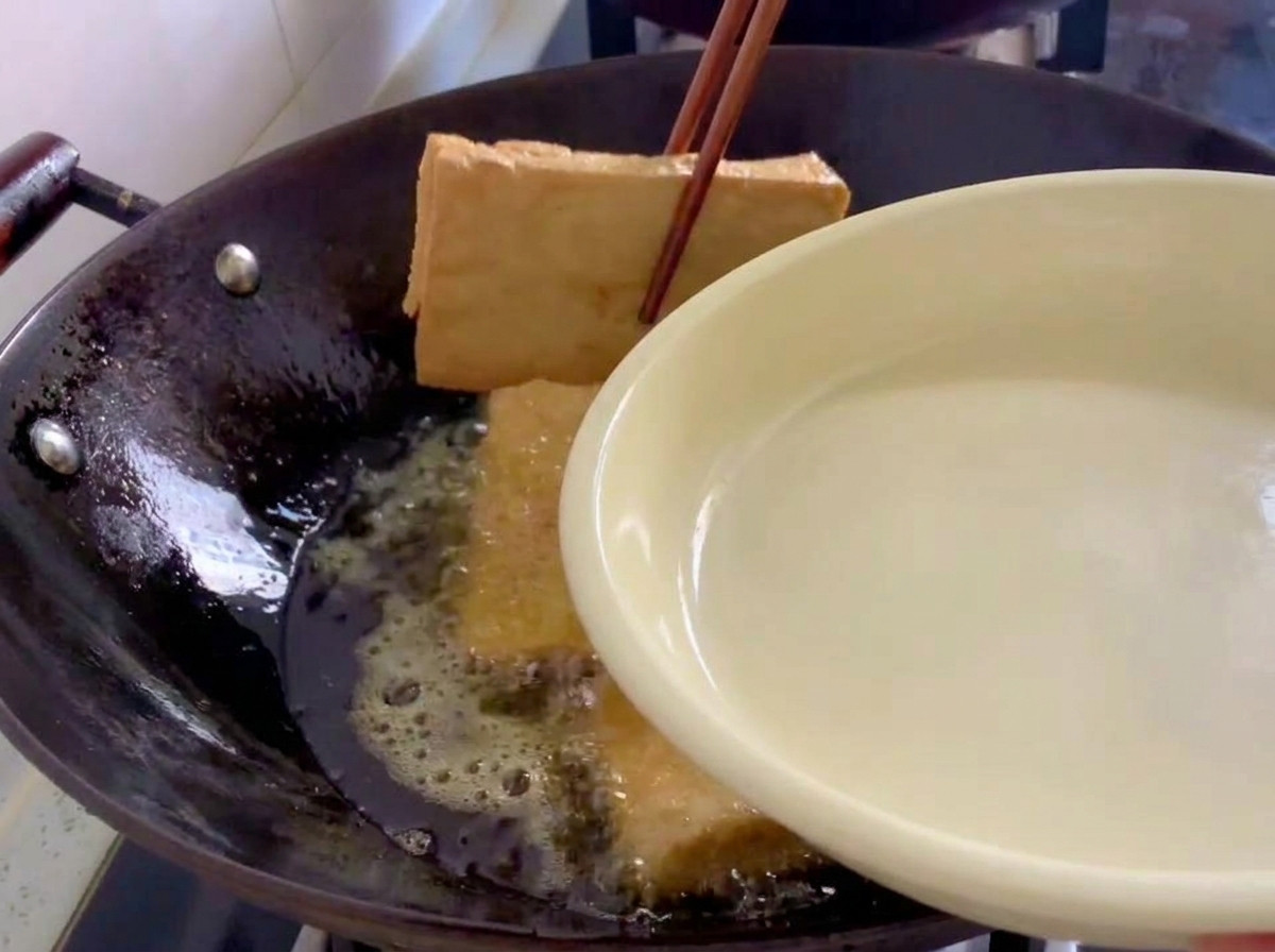 Blocs de tofu doré retirés dun wok à laide de baguettes en bois.