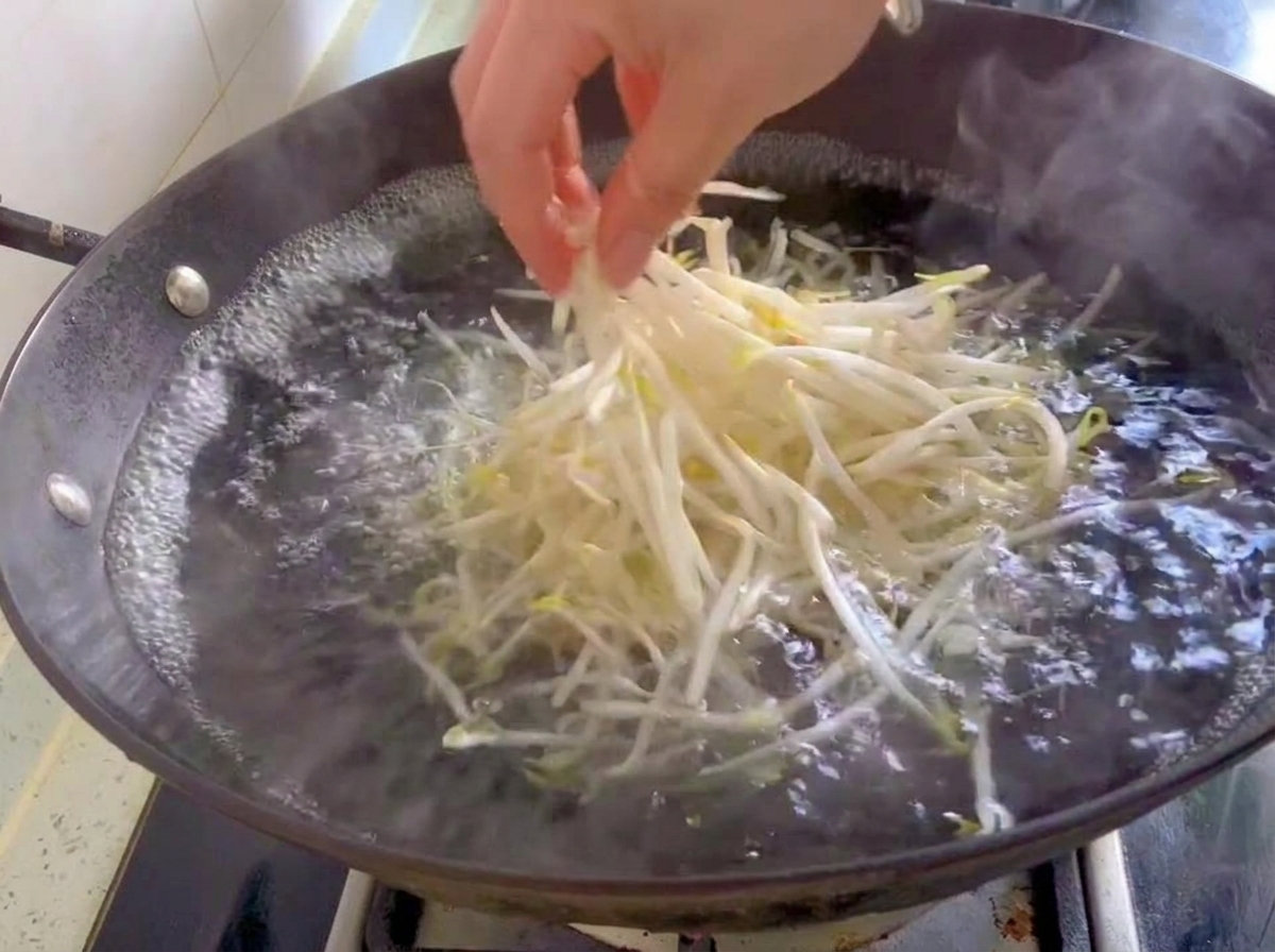 Une poignée de germes de soja frais et blancs plongée dans un wok deau bouillante.