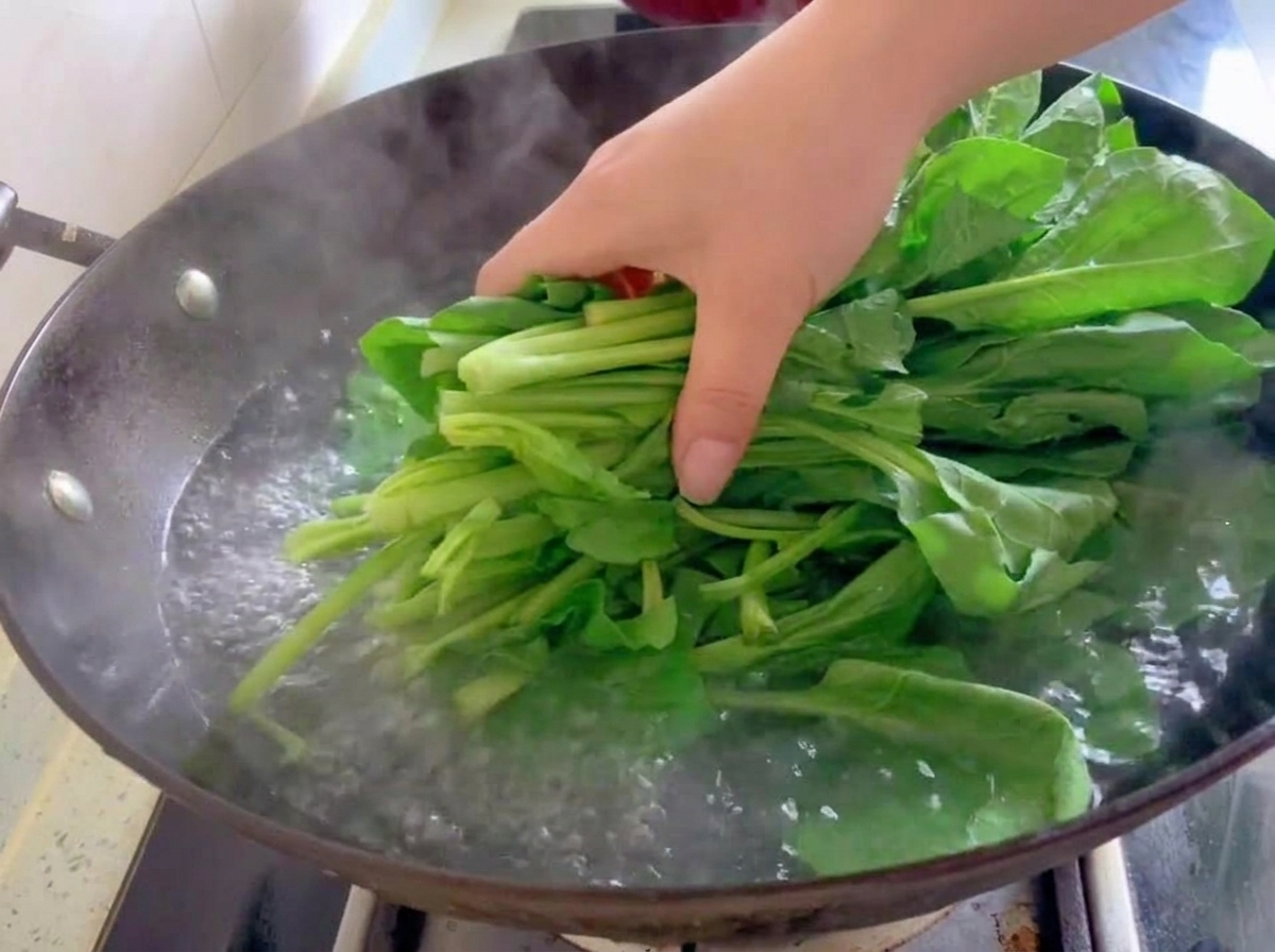 Un bouquet de feuilles dépinards frais plongé dans leau bouillante dun wok.