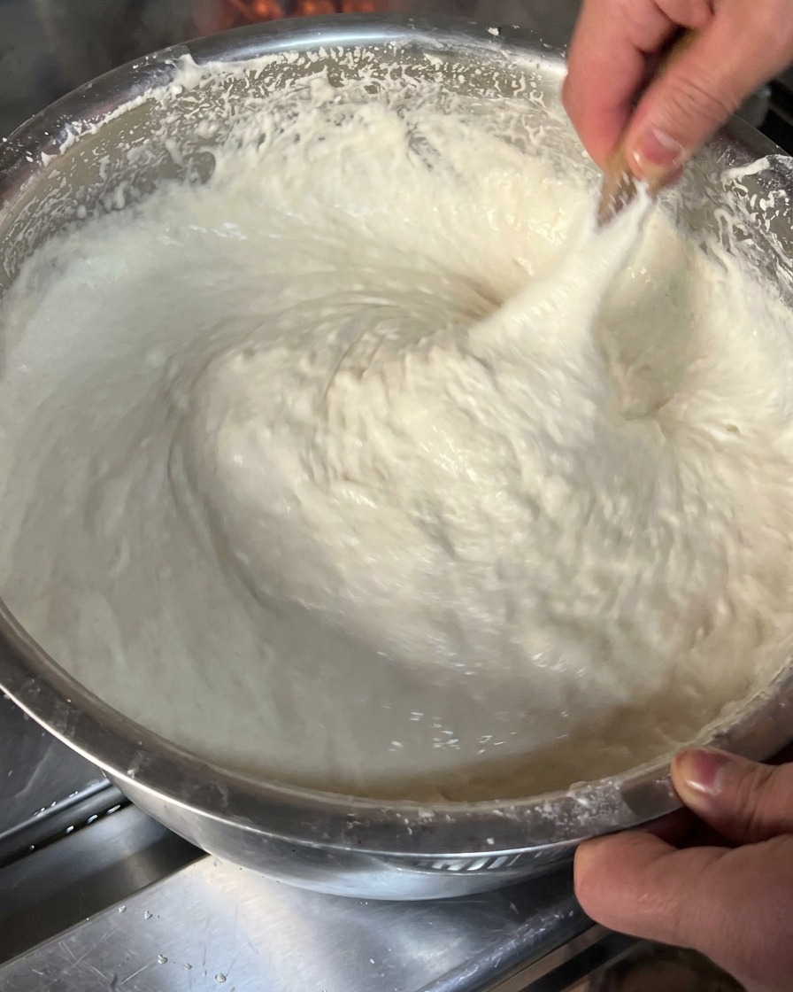 Gros plan sur une pâte blanche, épaisse et collante, soulevée et étirée à laide dun ustensile en bois dans un cul-de-poule.