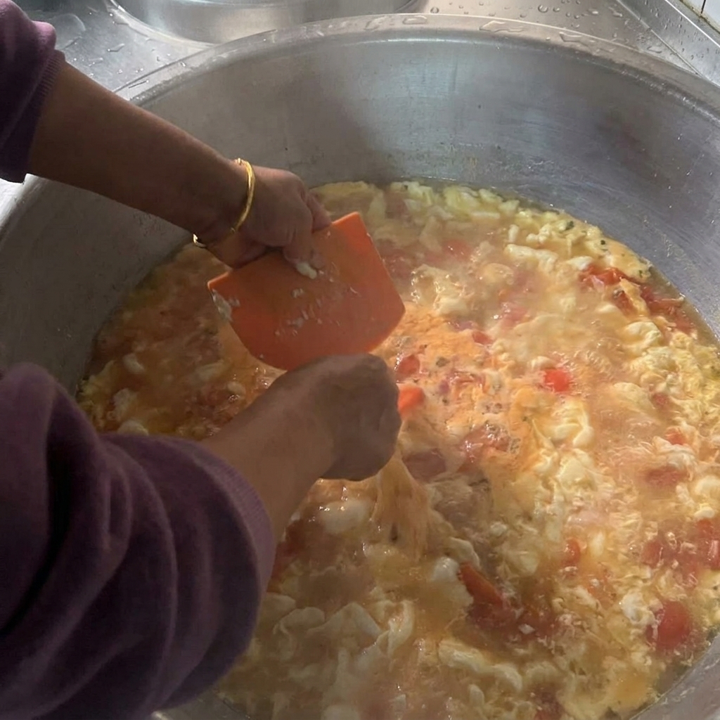Mains manipulant une corne en plastique orange pour détacher de petits morceaux de pâte humide au-dessus dune grande marmite de soupe frémissante.