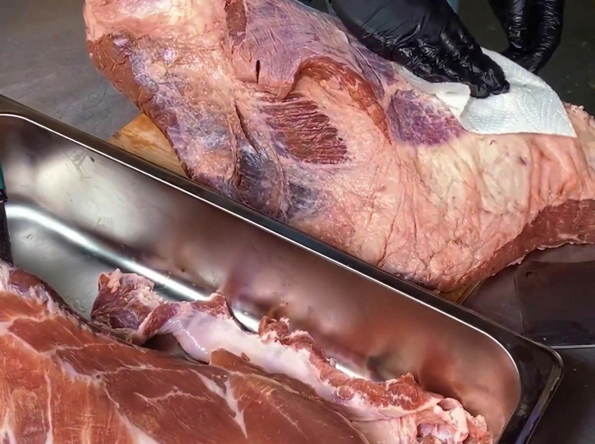 Un chef avec des gants noirs essuie une grande poitrine de bœuf crue sur une planche à découper en bois à laide dun essuie-tout blanc.
