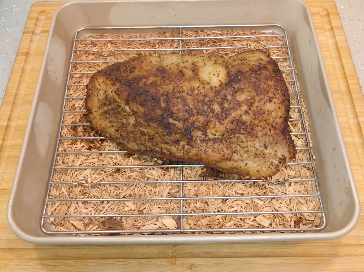 Une poitrine de bœuf chaude et assaisonnée reposant sur une grille métallique dans un plat de cuisson après le retrait du papier daluminium.