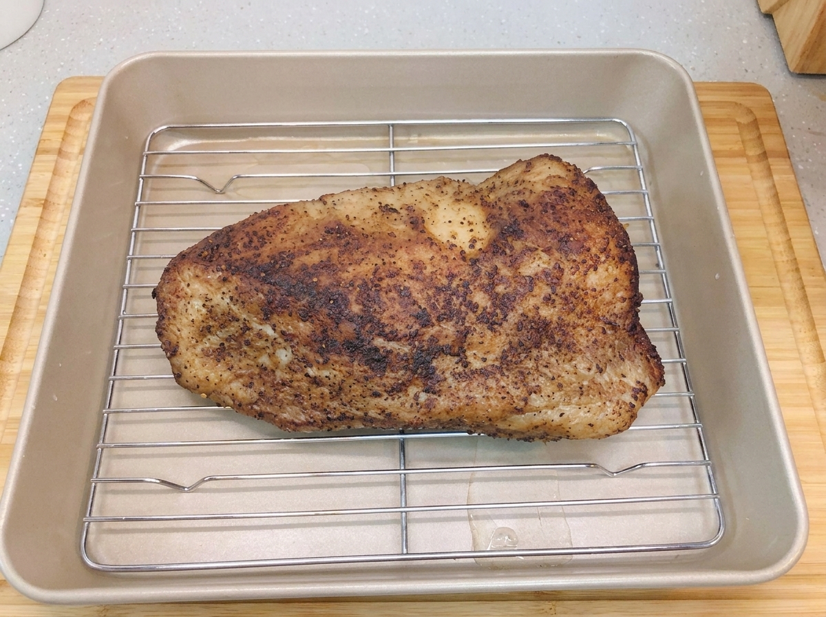 Une poitrine de bœuf saisie reposant sur une grille à lintérieur dun plat de cuisson doré contenant un fond deau.