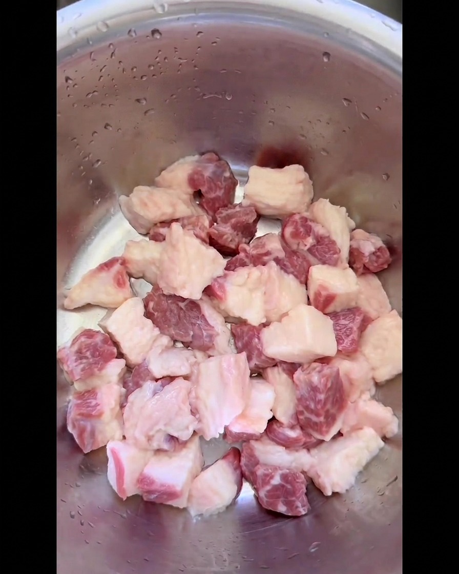 Morceaux de gras de poitrine de bœuf cru coupés en petits dés uniformes dans un bol en inox.