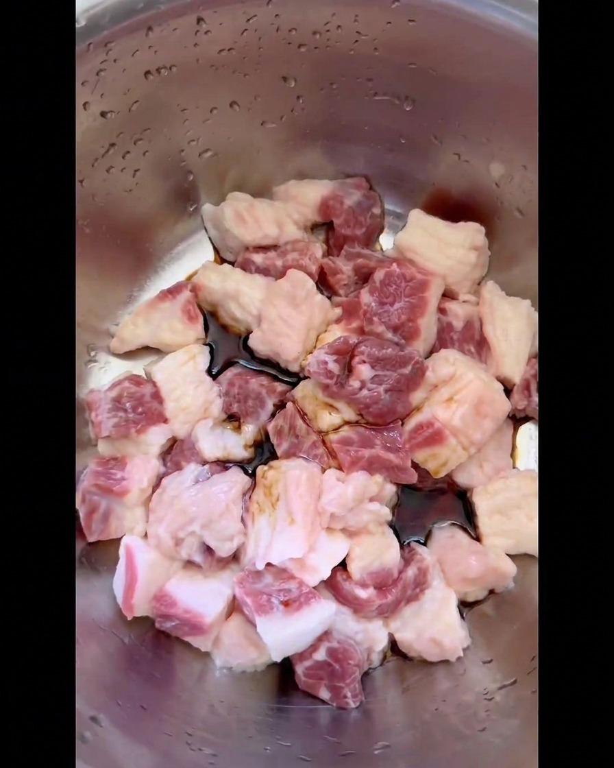 Sauce soja foncée et assaisonnements liquides versés sur les dés de gras de poitrine de bœuf cru dans un bol en inox.