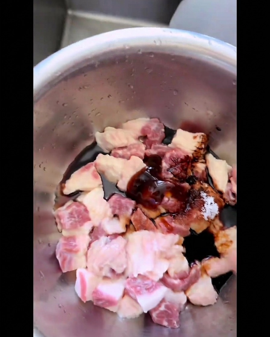 Morceaux de gras de poitrine de bœuf mélangés à la main avec de la sauce foncée, du sucre et du sel dans un bol en inox.
