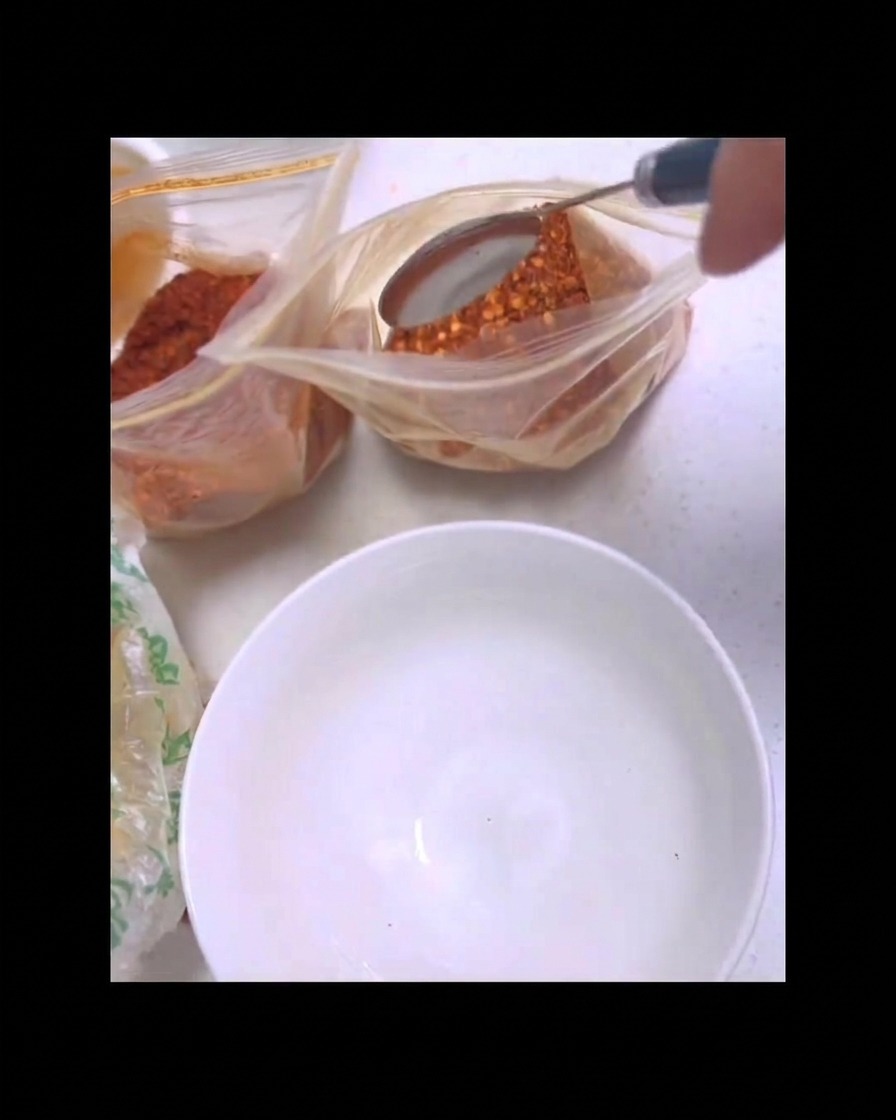 Une cuillère en métal prélevant du piment rouge en poudre dun sachet transparent au-dessus dun bol blanc.