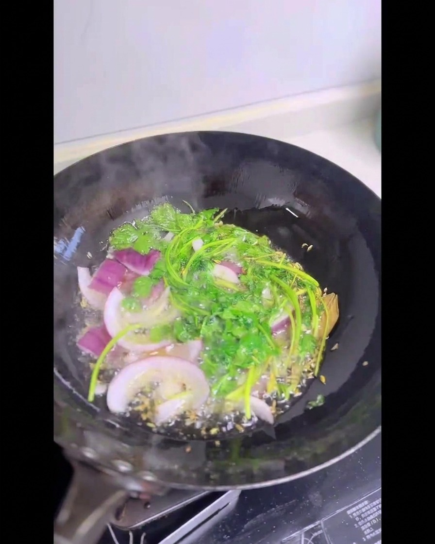 Tiges de coriandre fraîche et oignons rouges émincés crépitant dans un wok rempli dhuile chaude.
