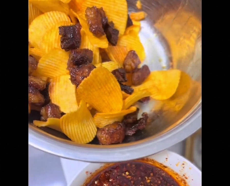 Morceaux de gras de bœuf croustillants tout juste sortis de lair fryer mélangés à des chips ondulées jaunes dans un grand bol en inox.