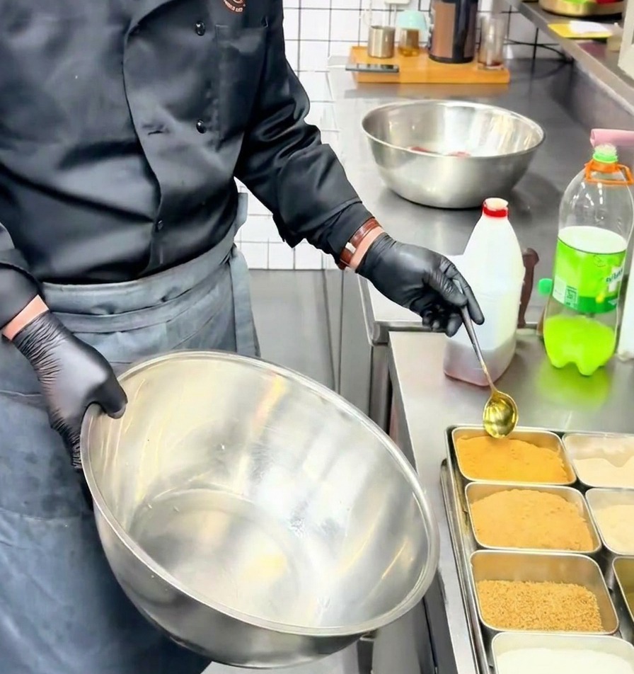 Un chef utilise une cuillère dorée pour verser du bouillon de bœuf en poudre dans un grand bol en inox.