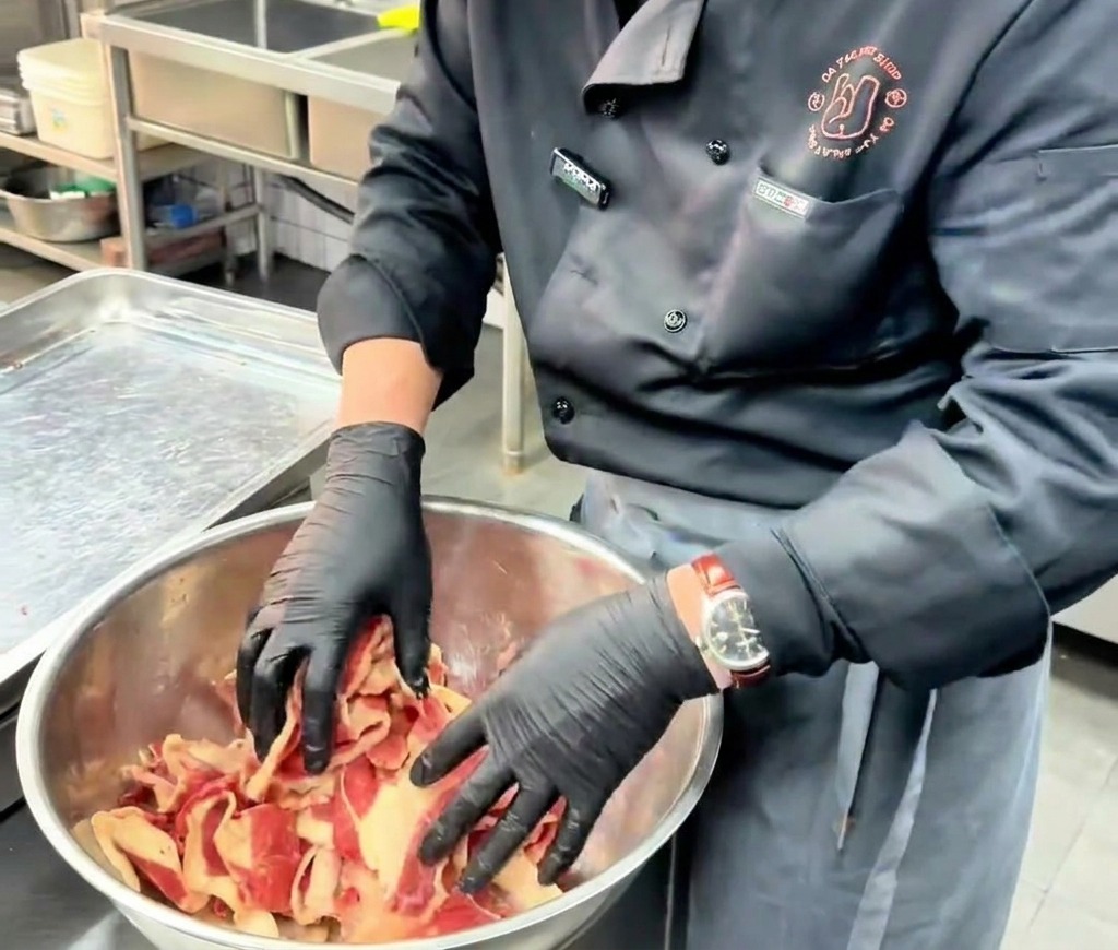 Un chef mélange délicatement à la main des tranches fines de bœuf avec la marinade dans un grand bol en inox.