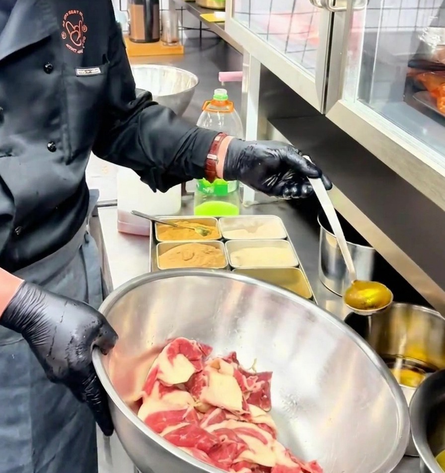 Une louche verse de lhuile assaisonnée dorée sur les tranches de bœuf marinées dans un bol en inox.