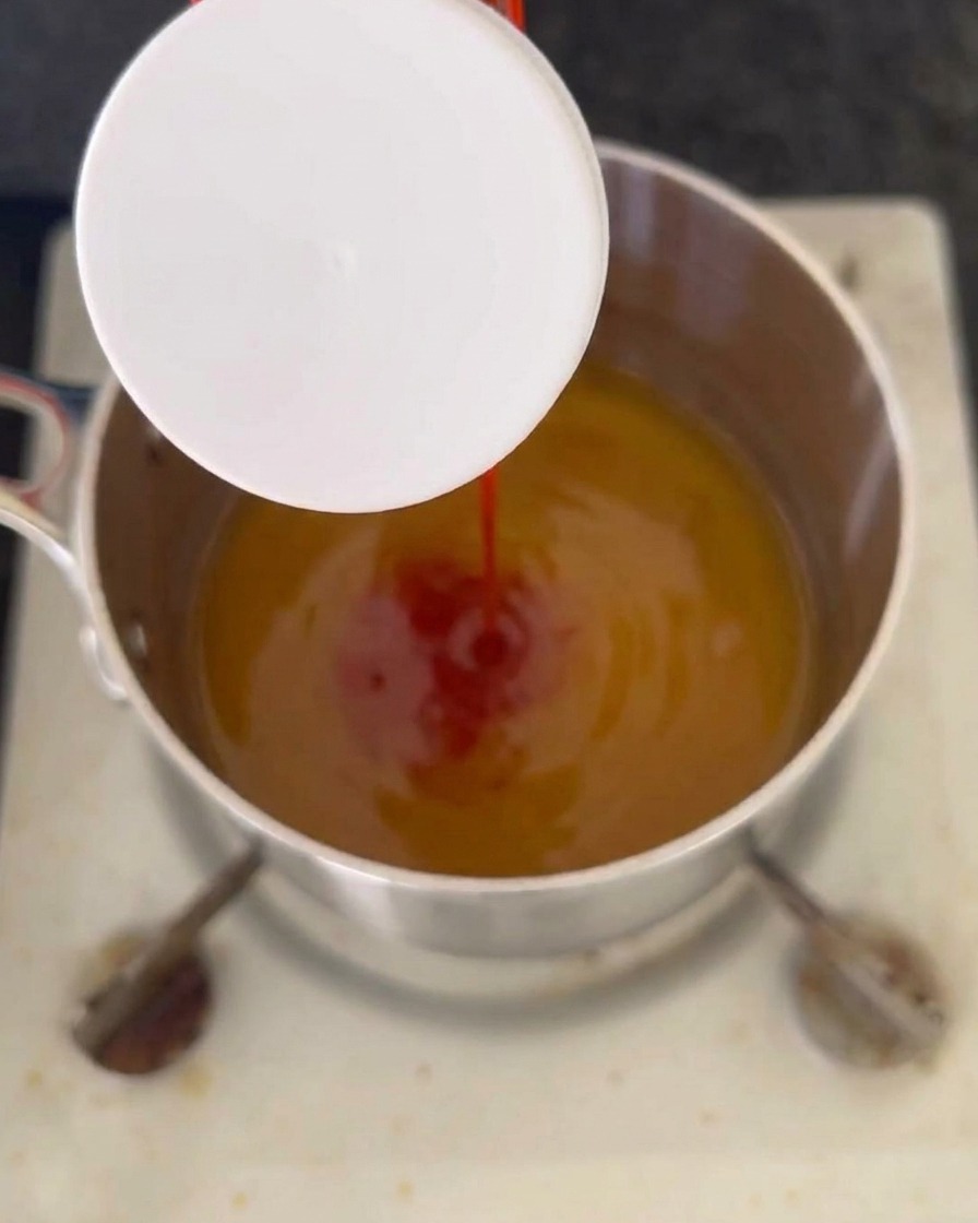 Un filet de ketchup rouge versé dans un mélange de liquide ambré qui frémit dans une casserole en acier inoxydable sur la cuisinière.