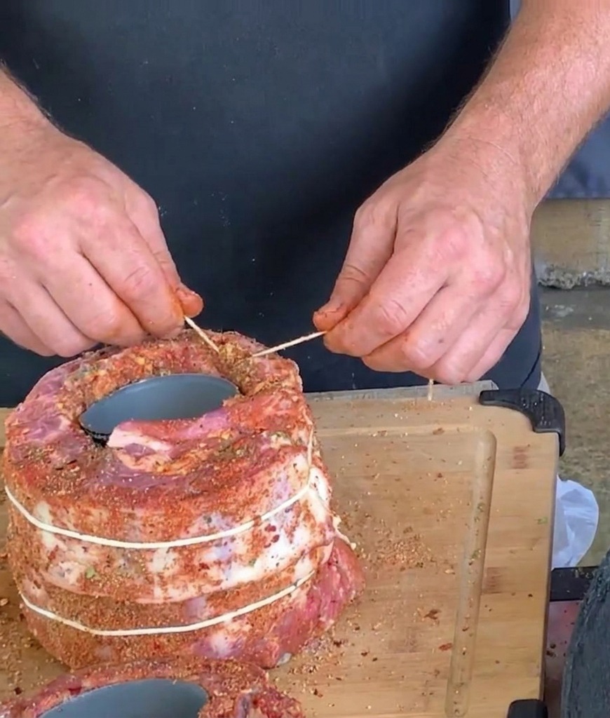 Des mains utilisant de la ficelle de cuisine blanche pour attacher et sécuriser un grand rouleau de ribs de porc autour dune canette.