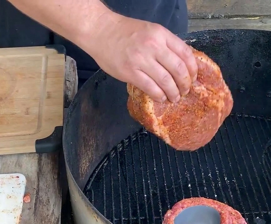 Une main déposant un panier de ribs ficelé et assaisonné sur la grille dun barbecue au charbon de bois pour une cuisson lente.
