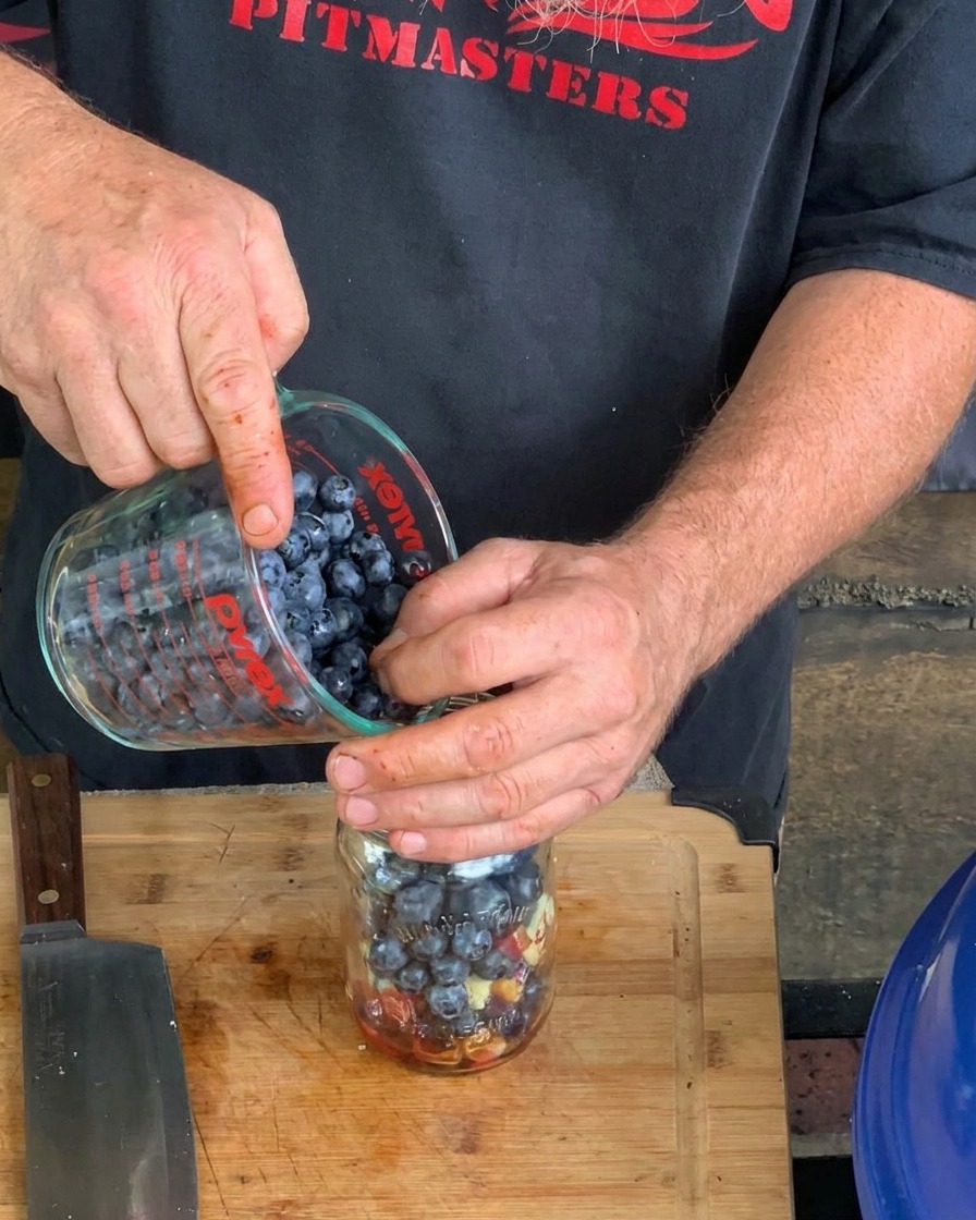 Gros plan sur des mains versant des myrtilles fraîches dun verre doseur dans un bocal en verre contenant les autres ingrédients de la sauce.