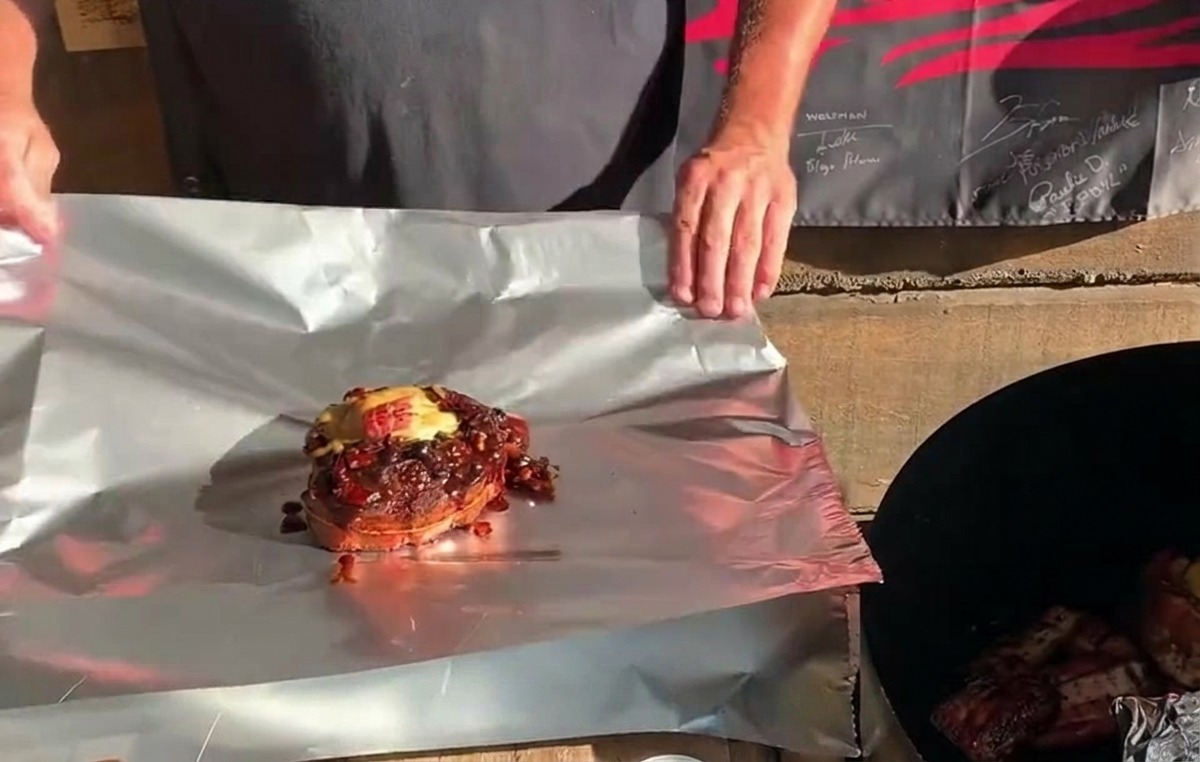 Un panier de ribs Saint-Louis entièrement farci, garni de fromage et de sauce, posé sur une feuille de papier daluminium prête à être repliée.