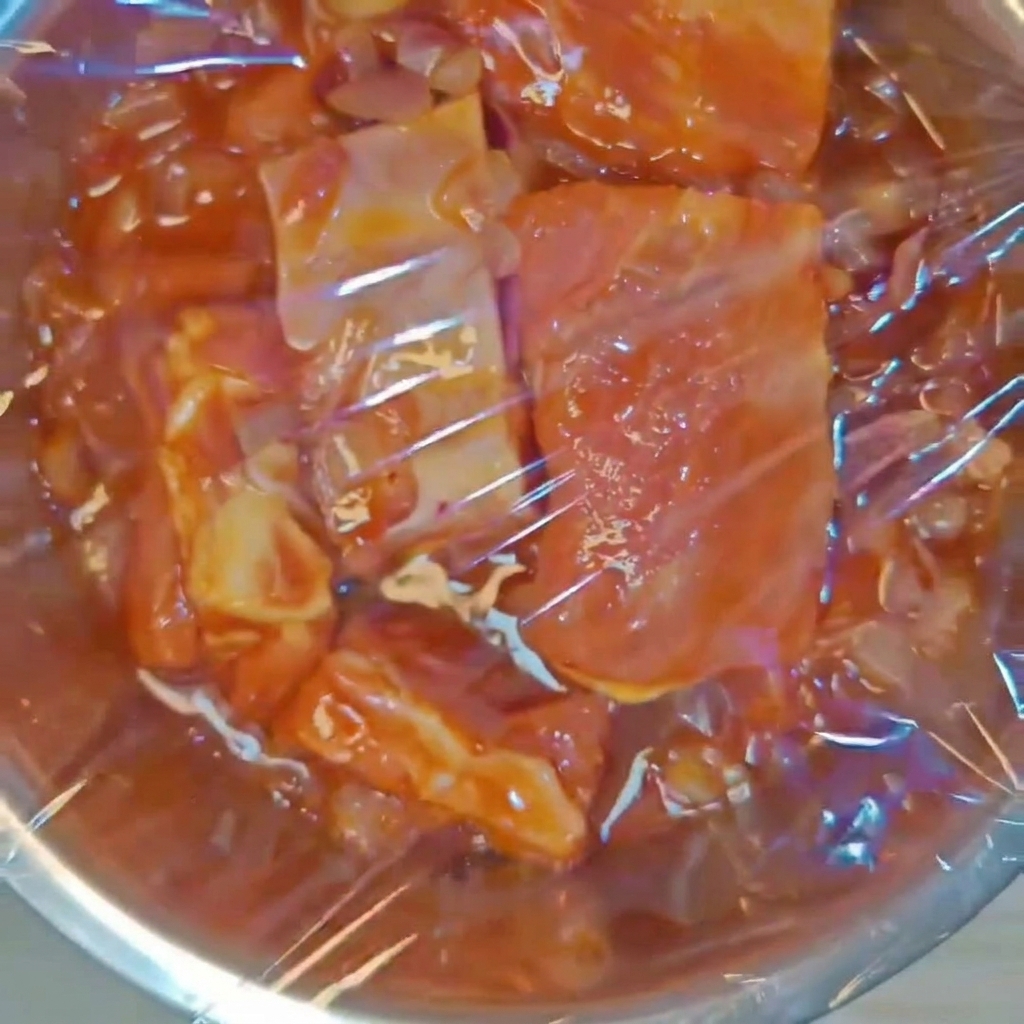 Un bol en métal contenant les travers de porc assaisonnés hermétiquement scellé avec du film étirable transparent.