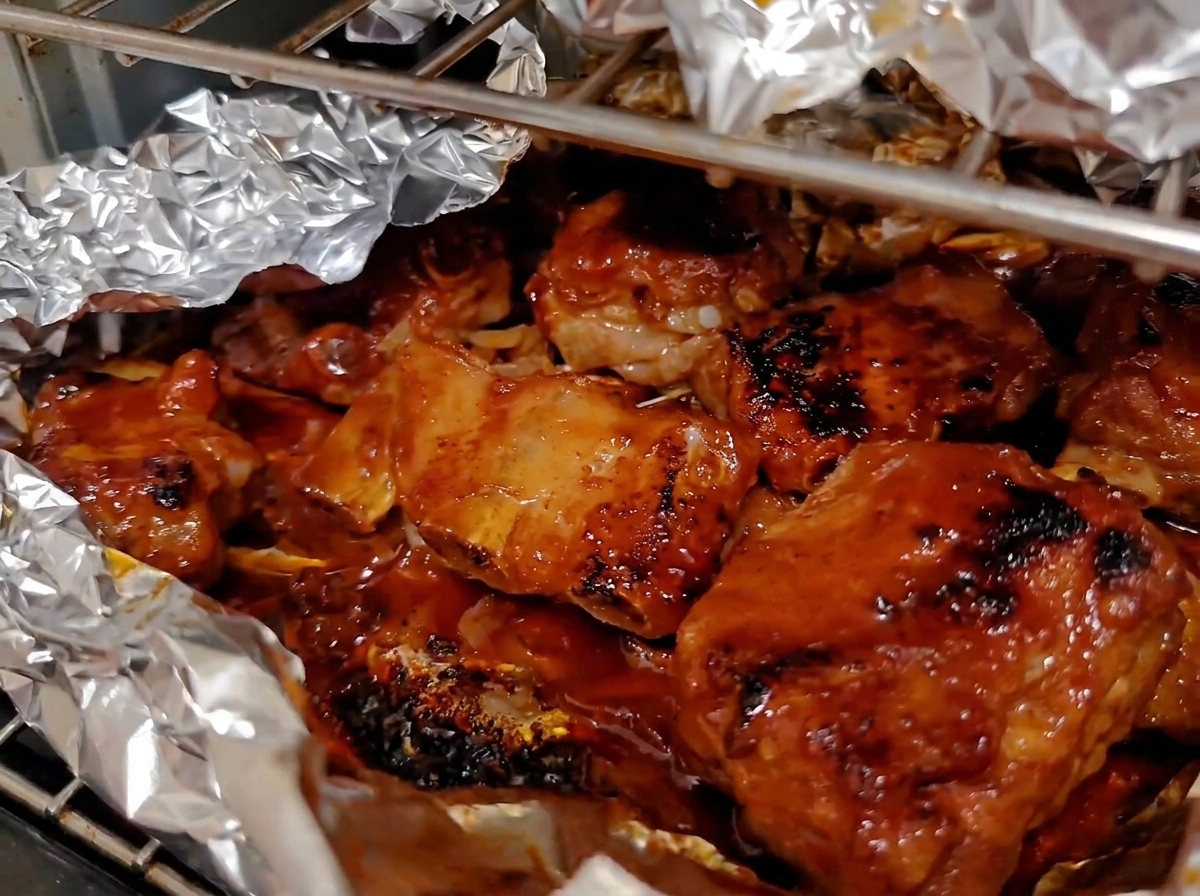 Travers de porc au four intensément caramélisés et laqués bouillonnant dans leur doublure de papier daluminium ouverte.