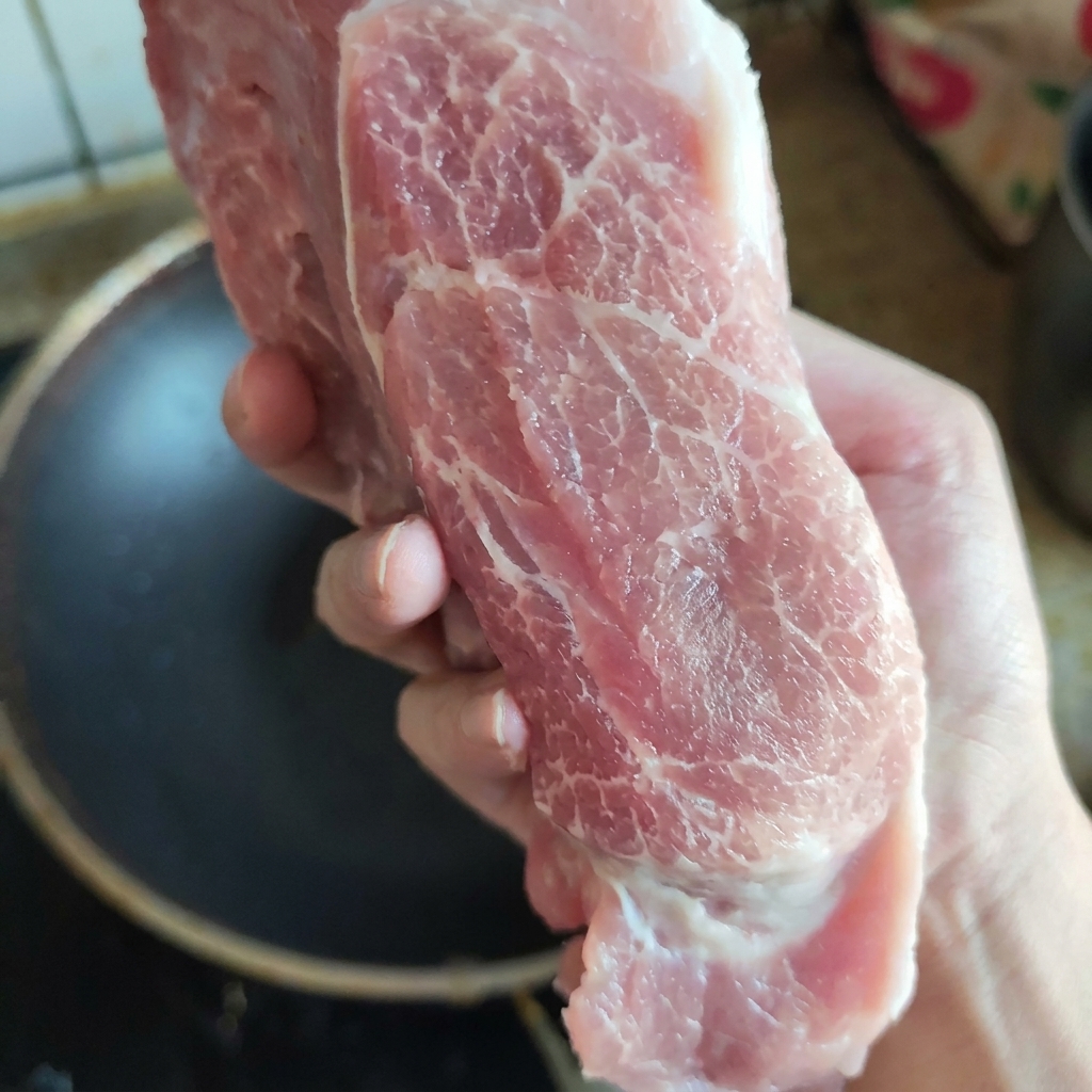 Un morceau de viande déchine de porc crue et bien persillée, présenté à la main pour montrer sa texture fraîche et sa répartition du gras.
