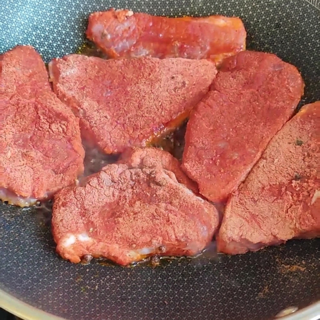 De tranches épaisses de porc enrobées dun mélange dépices rouges qui saisissent dans une poêle chaude sur le feu.