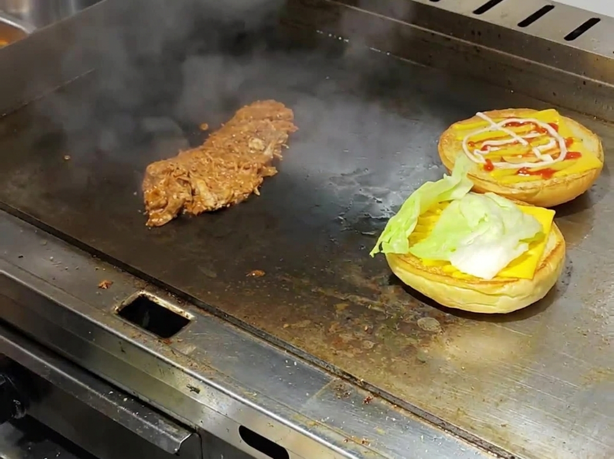 Des pains à burger toastés surmontés de fromage et de salade à côté du porc effiloché chaud sur une plaque de cuisson fumante.