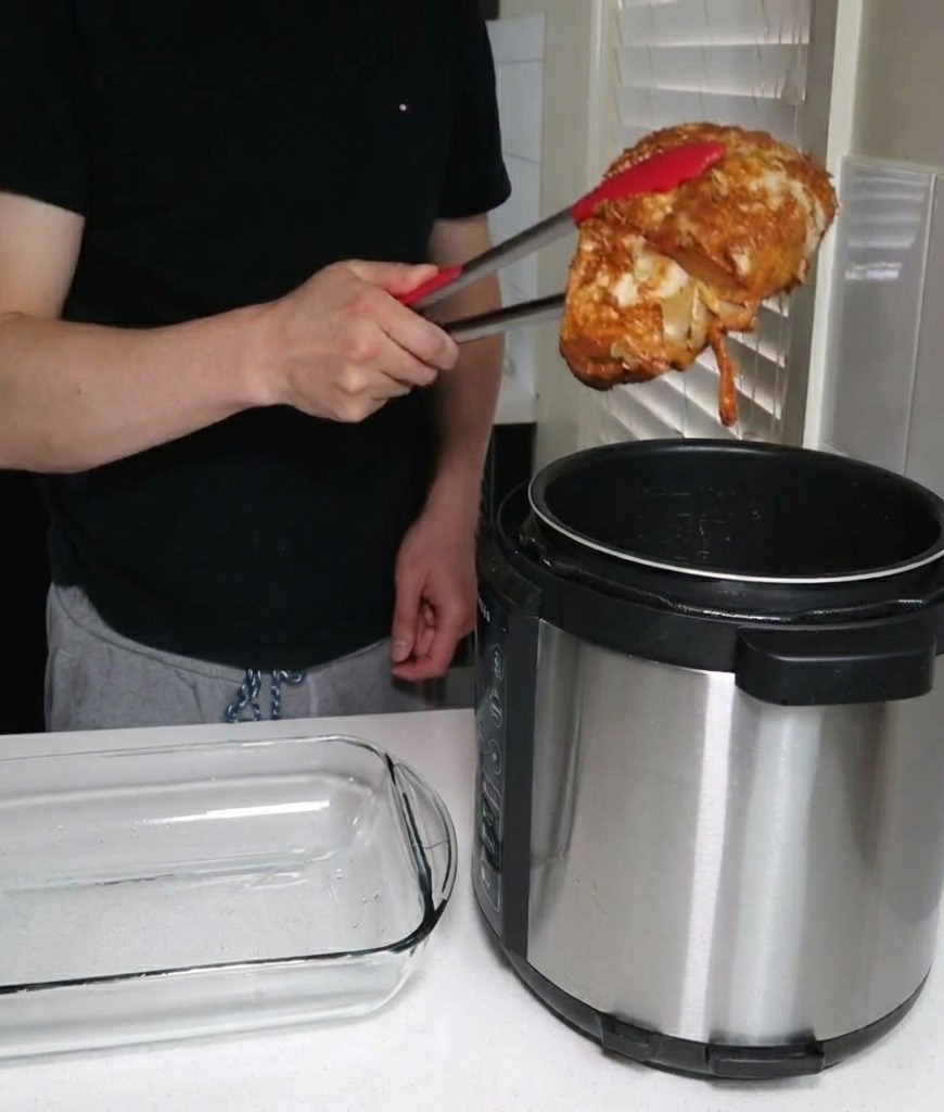 Une personne utilisant des pinces métalliques à embouts rouges pour sortir un gros morceau de porc cuit dun autocuiseur à côté dun plat vide.