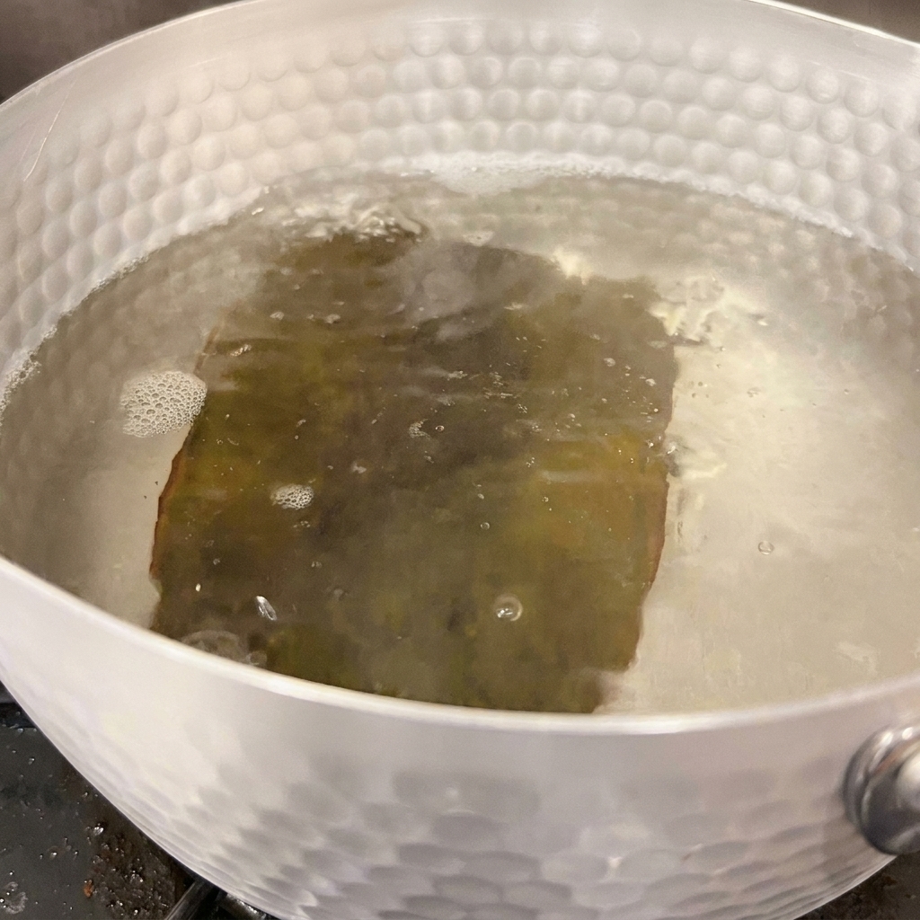Leau bout doucement autour dun morceau de kombu réhydraté à lintérieur dune casserole argentée sur le feu.