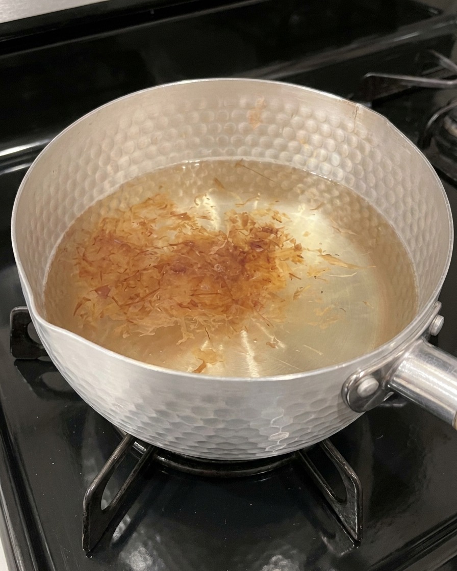 Des flocons de bonite légers et brun clair infusent à la surface dun bouillon chaud aux reflets ambrés dans une casserole.