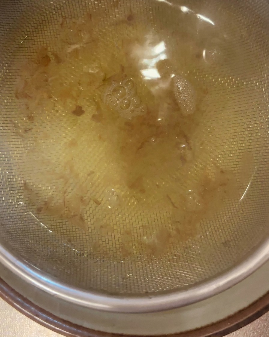 Un bouillon dashi doré et limpide est filtré à travers une passoire fine en acier inoxydable dans un bol placé en dessous.