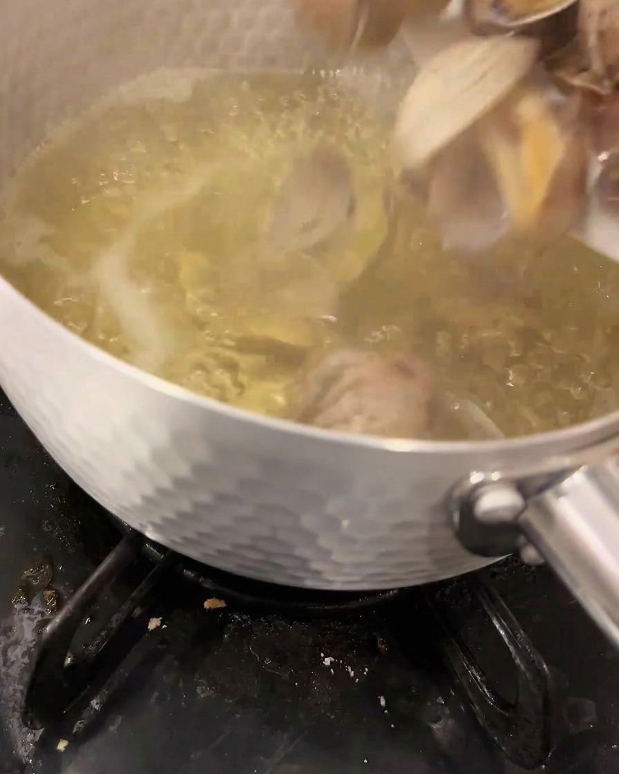 Des palourdes fraîches sont plongées dans un bouillon dashi frémissant et clair à lintérieur dune casserole métallique sur un réchaud à gaz.