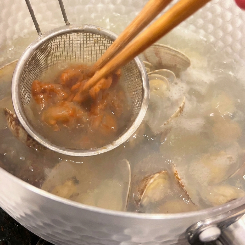 Une petite passoire à main retient la pâte miso brune tandis que des baguettes la mélangent à la soupe aux palourdes bien chaude.