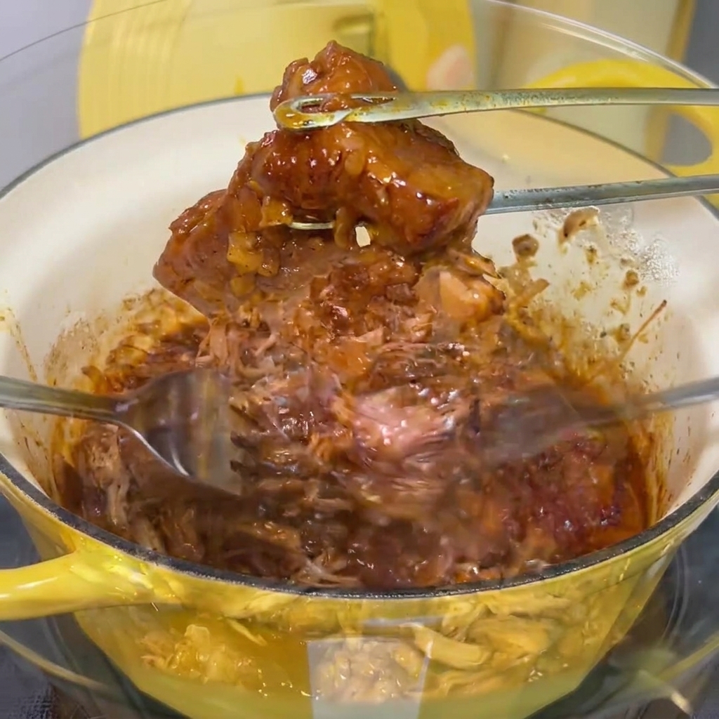 Le porc est effiloché avec deux fourchettes dans un bol en verre.