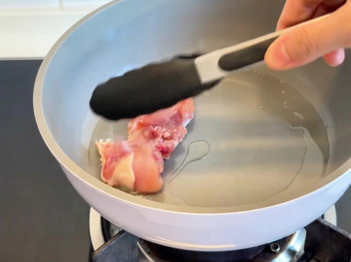 Cuisses de poulet cuites côté peau dans une poêle chaude, révélant une peau croustillante et dorée.