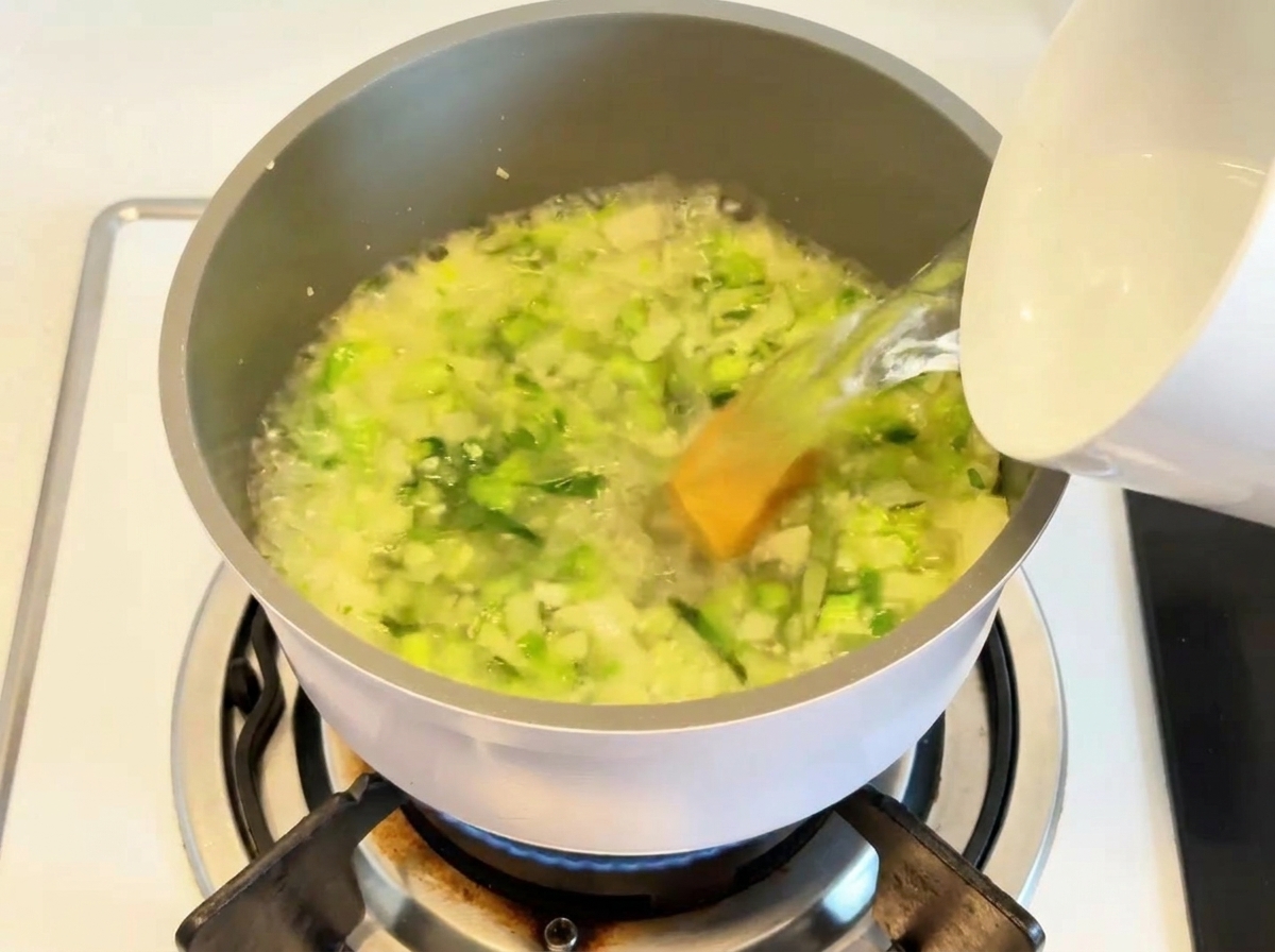Eau versée dans une marmite contenant des légumes revenus et un fond de bouillon.