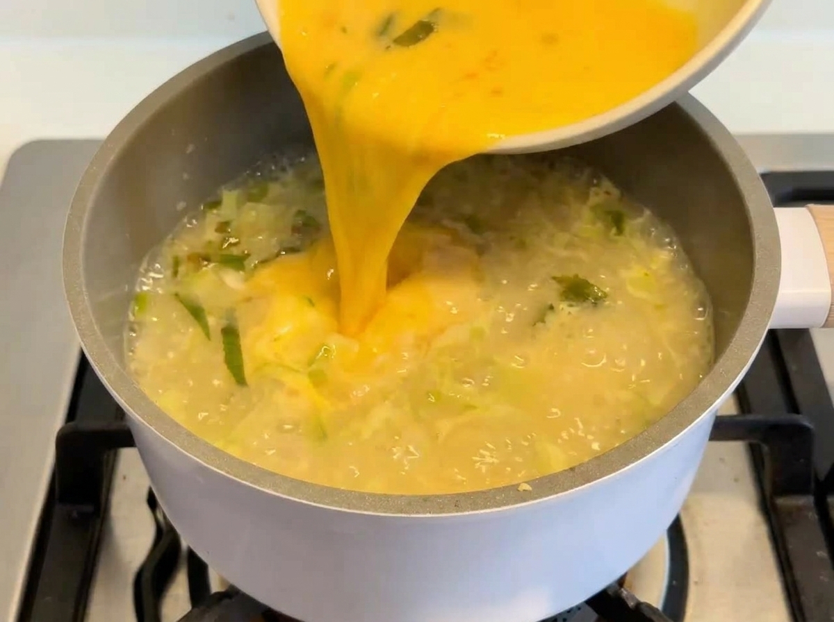 Mélange éclatant dœufs et de citron versé dun bol blanc dans une marmite frémissante de soupe veloutée.