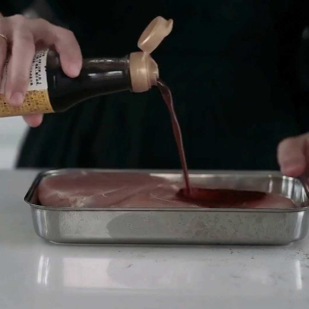 Morceaux de blanc de poulet juteux dans un plateau en métal, entièrement enrobés dune marinade liquide savoureuse.