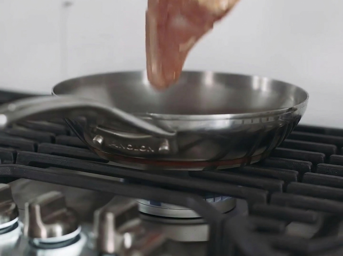 Un blanc de poulet en train de dorer dans une poêle en acier inoxydable sur une plaque de cuisson.