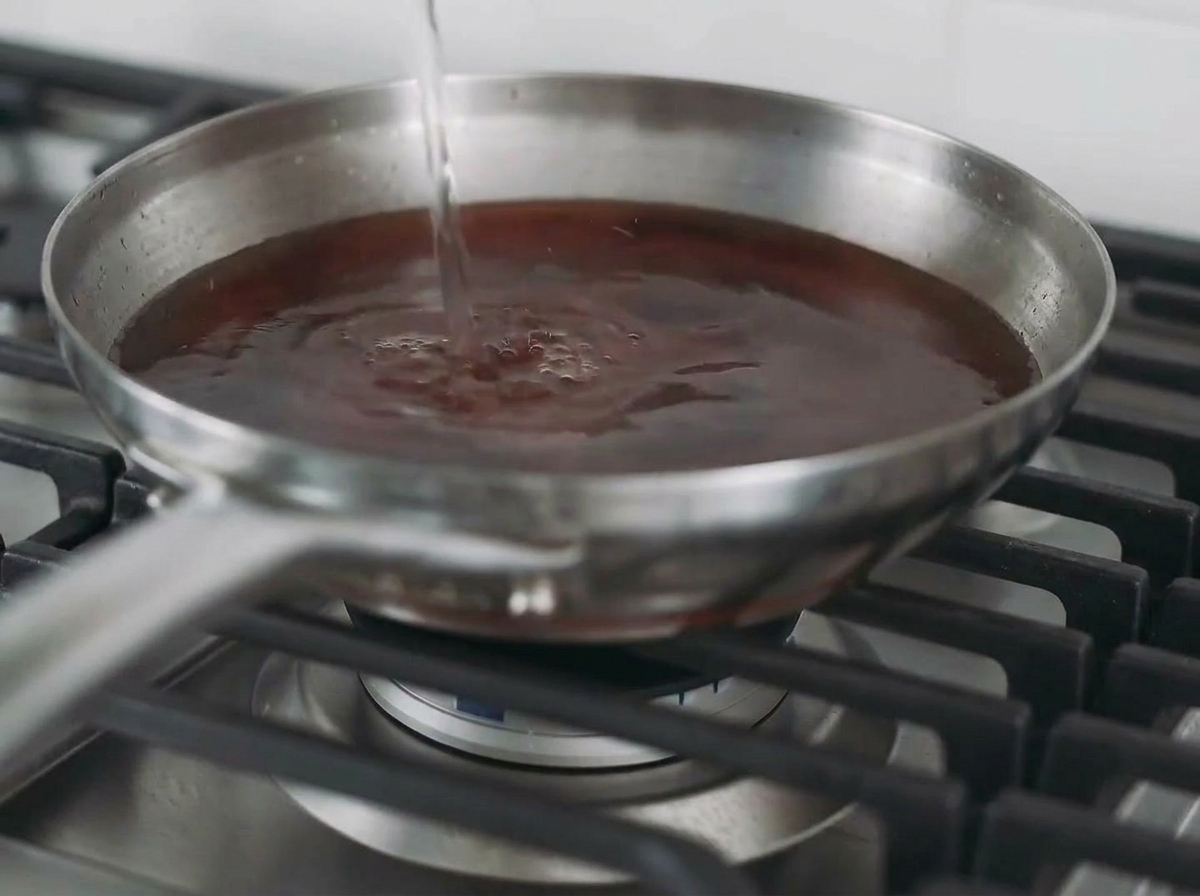 Du liquide versé dans une poêle contenant un blanc de poulet poêlé pour créer un bouillon.
