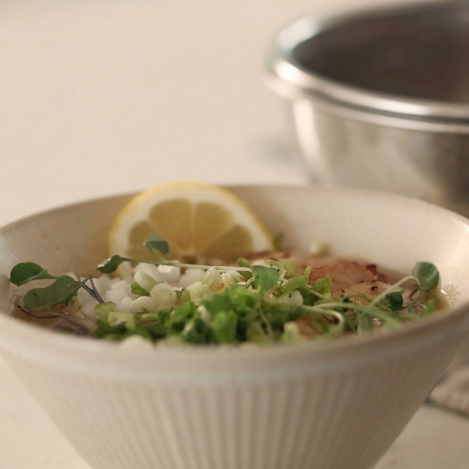 Un bol de nouilles froides dans un bouillon surmonté doignons en dés, doignons verts et de poivre noir.
