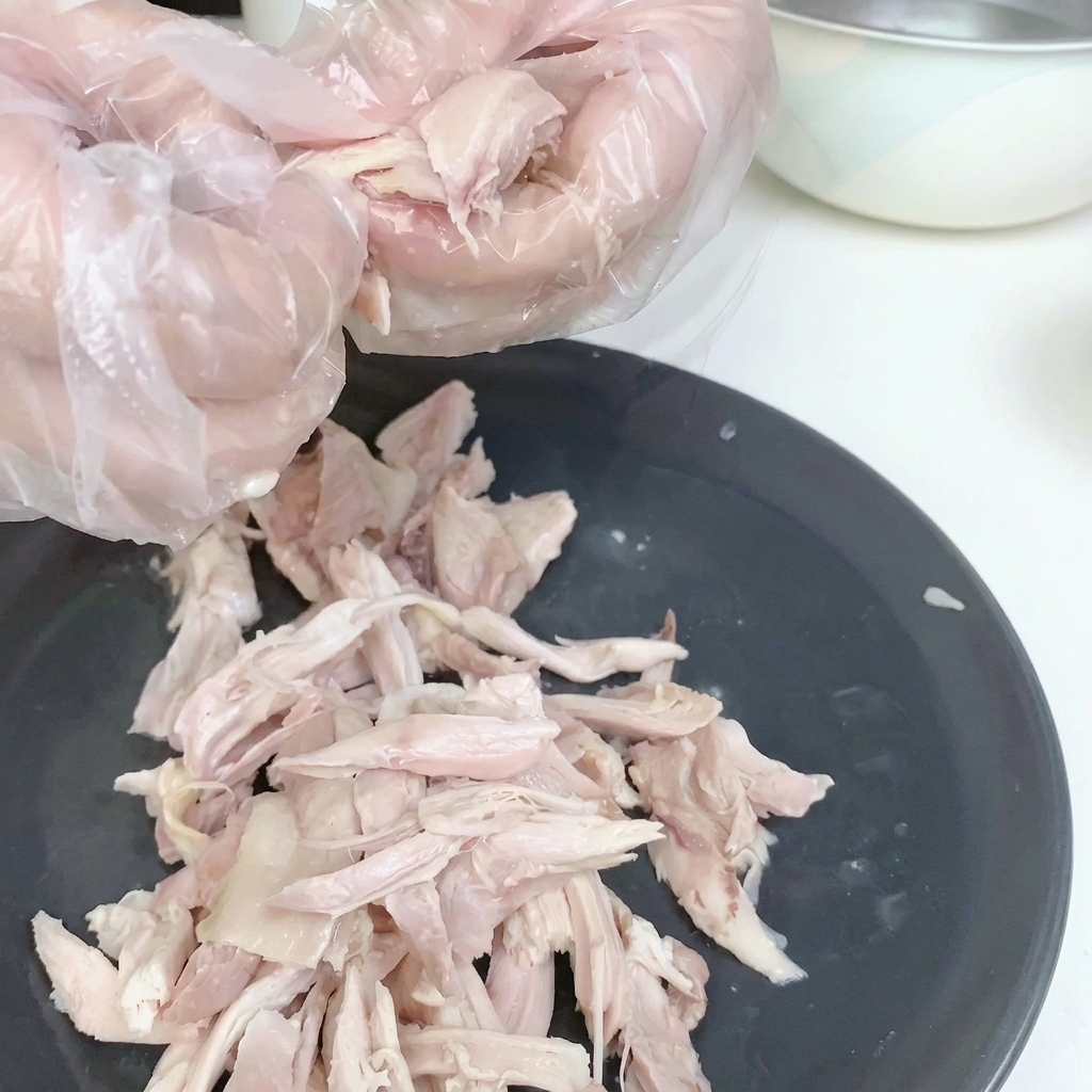 Viande de poulet effilochée sur une assiette blanche, peau retirée.